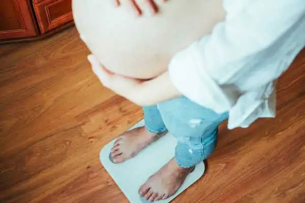 Image of woman weighing herself and experiencing weight gain through pregnancy Aberdeen